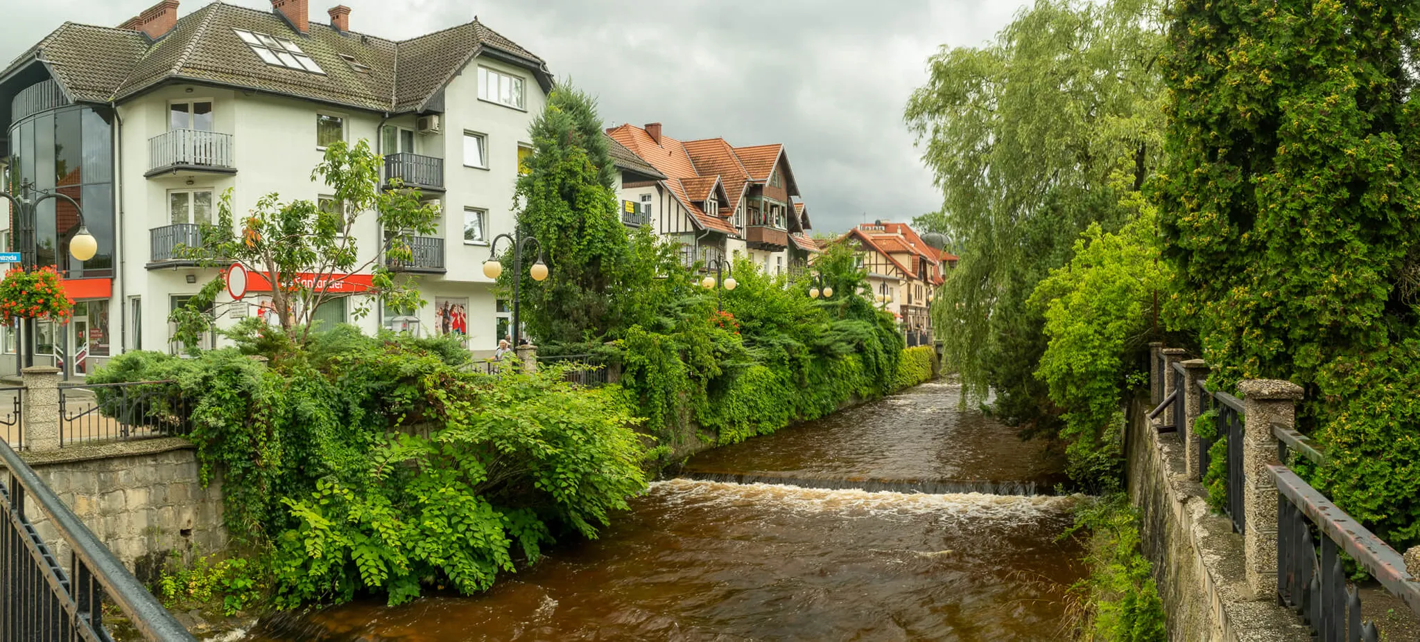 Panorama rzeki Bystrzycy Dusznickiej z zabytkową zabudową uzdrowiska Polanica Zdrój i bujną zielenią