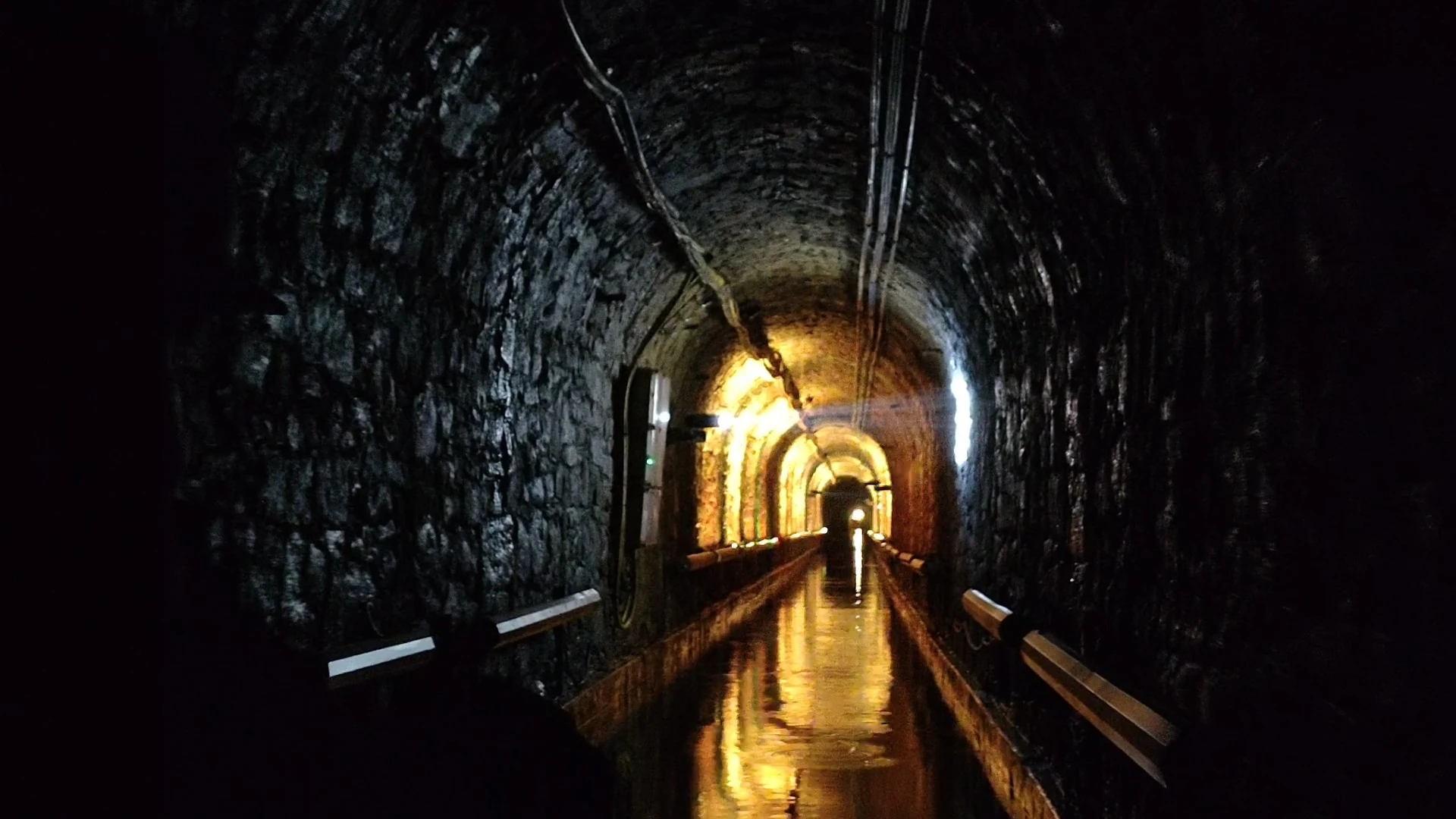 Oświetlony tunel podziemnego spływu w Sztolni Luiza Zabrze Zalany tunel z ciepłym oświetleniem odbitym w wodzie podczas podziemnego spływu w Sztolni Luiza w Zabrzu